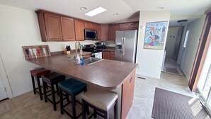 A modern kitchen with wooden cabinets, stainless steel appliances, and a central island with bar stools. - Silver Lake - 4th of July - Lake Access - MIS (Addison)