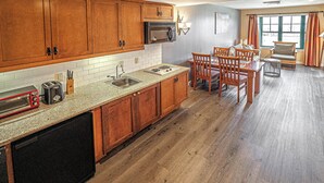A kitchen with wooden cabinets, a microwave, a sink, and a dining area with chairs. - Mountain Creek Lovely 1 Bedroom/Pool/Jacuzzi/King Bed/Ski In/Out (Vernon Township)
