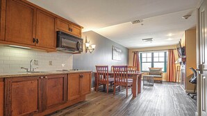 A kitchen with wooden cabinets, a microwave, and a dining area with chairs and a table. - Mountain Creek Lovely 1 Bedroom/Pool/Jacuzzi/King Bed/Ski In/Out (Vernon Township)