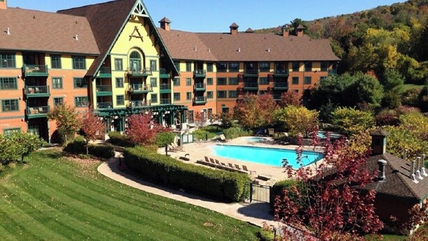 A hotel with a swimming pool, green lawns, and a hilly backdrop. - Mountain Creek Lovely 1 Bedroom/Pool/Jacuzzi/King Bed/Ski In/Out (Vernon Township)