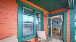 A covered porch with two chairs and a table, a sliding glass door leading inside, and a view of the interior with a couch and a painting. - Mountain Creek Lovely 1 Bedroom/Pool/Jacuzzi/King Bed/Ski In/Out (Vernon Township)