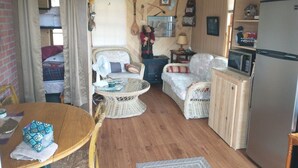 A compact living space with a dining table, two wicker chairs, a small round table, a microwave, and a refrigerator. - Quaint cozy little cabin geared for folks coming to Leech Lake to fish or relax. (Federal Dam)