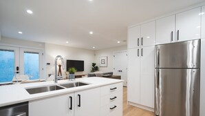 A modern kitchen with white cabinetry, a stainless steel refrigerator, and a built-in sink.