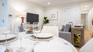 A dining area with a table set for four, including wine glasses and plates, in a modern living room with a sofa and a TV.