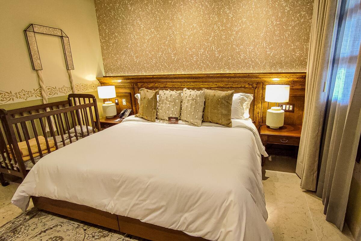 A hotel room with a large bed, two bedside tables with lamps, a wooden headboard, and a patterned wallpaper.
