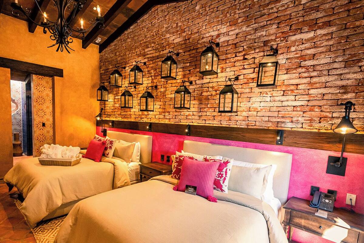A hotel room with two beds, a brick wall, and hanging lanterns.