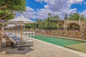 Zona de piscina con sillones de descanso y sombrillas, rodeada de muros de piedra y vegetación.