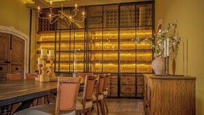 Un comedor con una larga mesa de madera, varias sillas, una araña y un jarrón decorativo con flores.