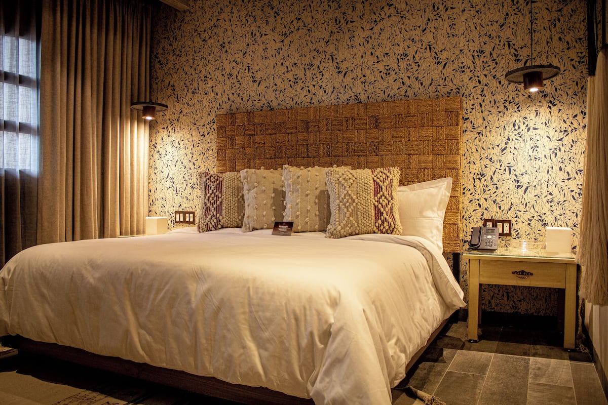 A neatly made bed with a wooden headboard, two bedside tables with lamps, and a patterned wallpaper.