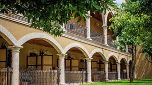 Un edificio con un patio cubierto, que cuenta con paseos con arcos y columnas, y un área cercada con plantas en macetas.