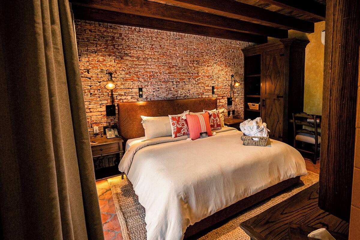 A bedroom with a brick wall, wooden headboard, and a bed with white bedding and red pillows.