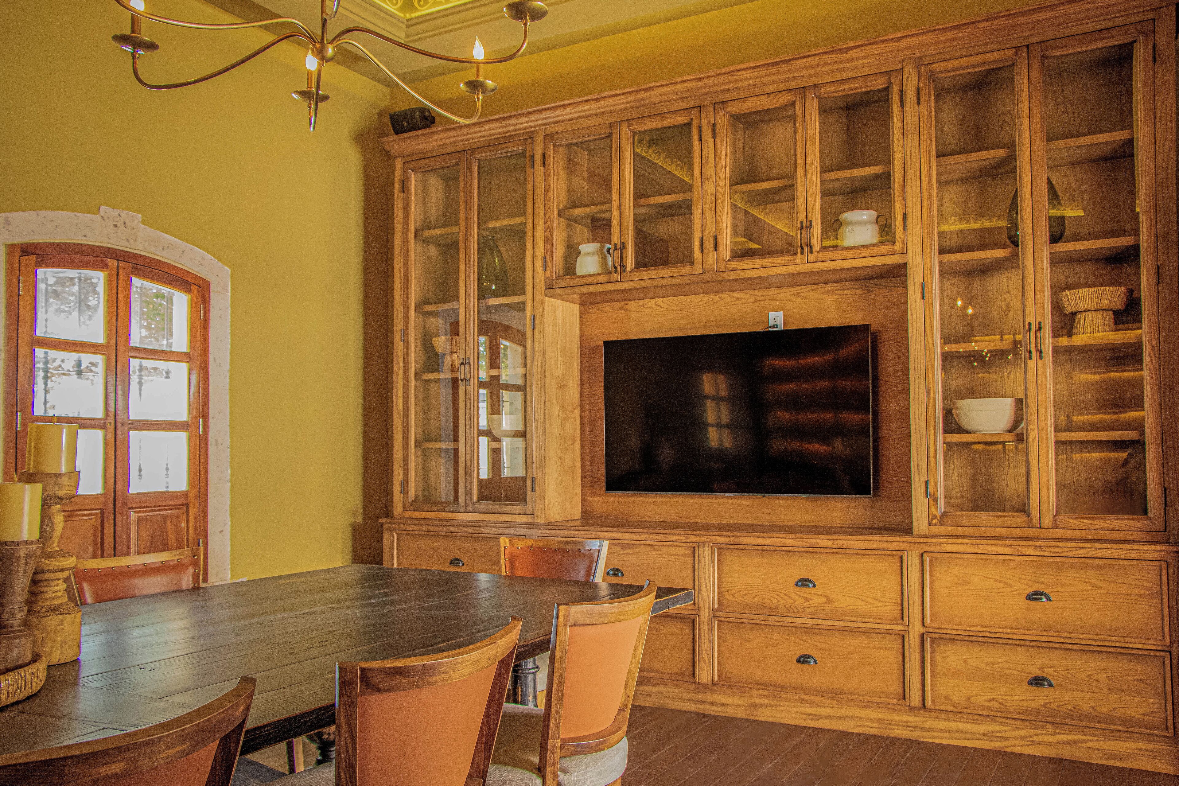 A dining area with a wooden table and chairs, a built-in TV, and wooden cabinets with glass doors.