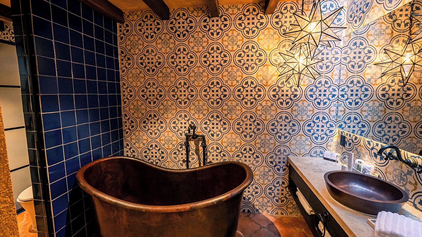 Un baño con una bañera independiente, un lavabo y un pared con azulejos estampados.