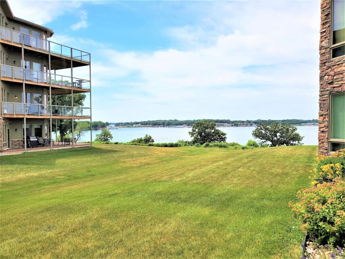 A residential property with a grassy lawn, a balcony with outdoor furniture, and a view of a body of water.