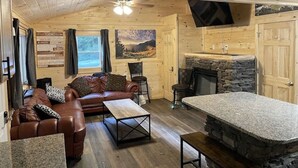 Ein gemütliches Blockhaus-Interieur mit Holzbalkendecke, Kamin aus Stein, braunem Leder Sofa und Esstisch.