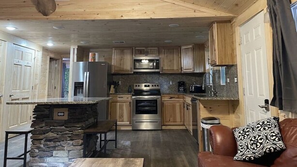 Ein Ferienhaus-Interieur mit Kamin aus Stein, Holzschränken, einer Küche mit Edelstahlgeräten und einem Ledersofa.