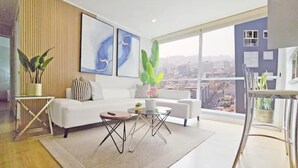 A modern living room with a white sofa, a coffee table, and a view of the city through large windows. - BEST LOCATION BALCONY! MIRAFLORES HEART 1BD/1.5BA (Miraflores)