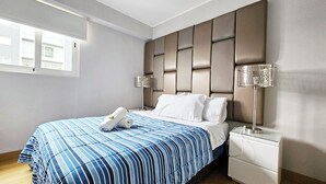 A modern hotel room with a large bed, a headboard with a padded design, two bedside lamps, and a window providing natural light. - BEST LOCATION BALCONY! MIRAFLORES HEART 1BD/1.5BA (Miraflores)