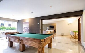 A pool table in a common area with a modern design, a dining table with chairs, and a television in the background.