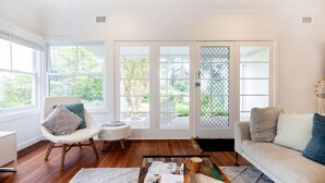 A bright living room with a white couch, a wicker chair, a small table, and a magazine on the floor.