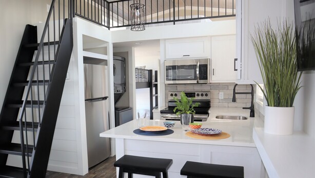 Une cuisine moderne avec des meubles blancs, un îlot central doté de tabourets, un four à micro-ondes et une cuisinière.