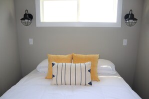 Une chambre à coucher avec un lit, deux lampes fixées au mur et une fenêtre située au-dessus du lit.