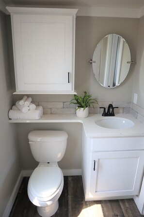 Une salle de bain comprenant des toilettes, un lavabo, un miroir et un meuble de rangement.