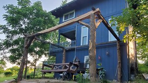 Een blauw huis met een houten schommel en een bank in de achtertuin.