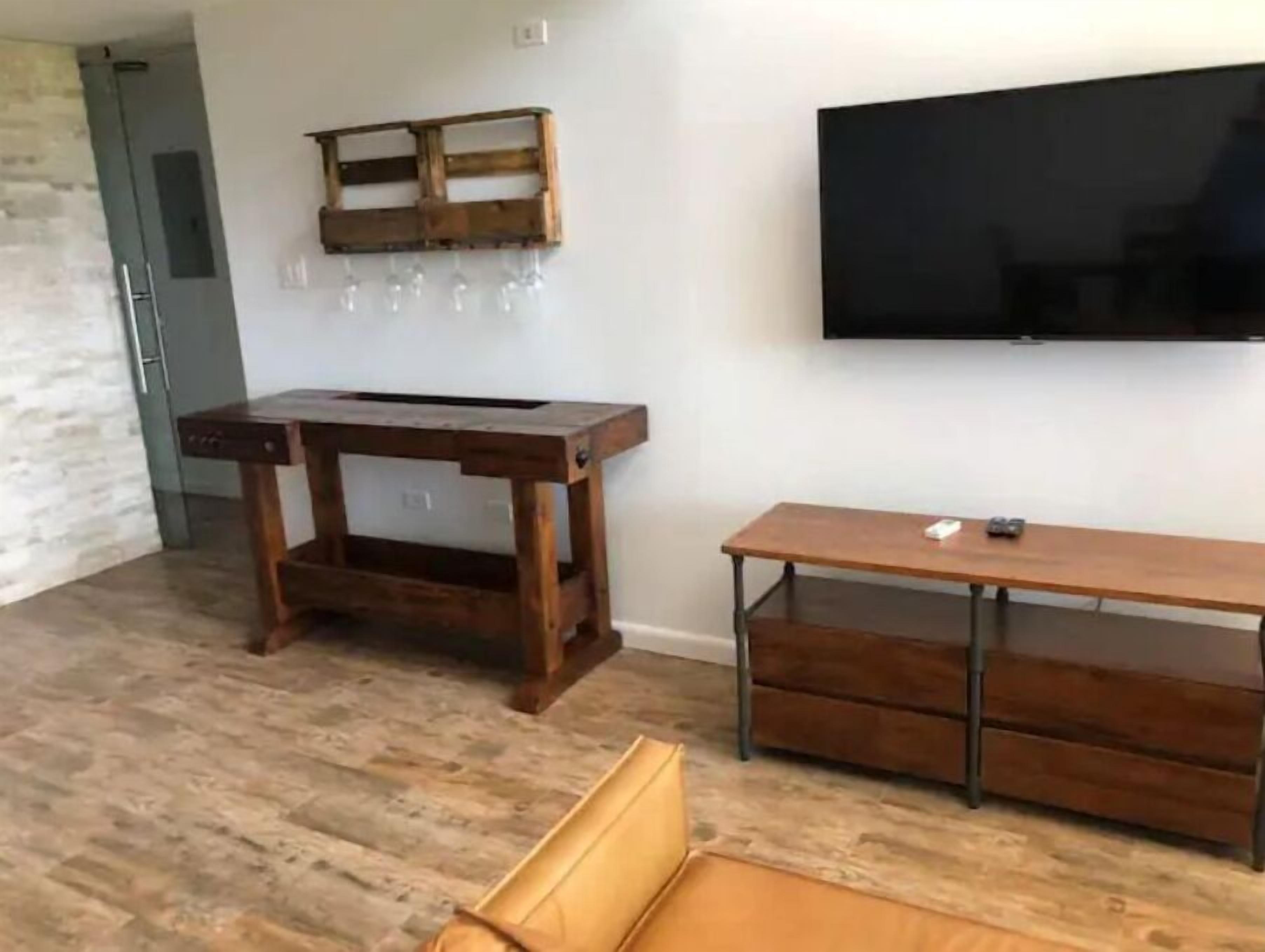 Ein Zimmer mit einem Holztisch, einem an der Wand montierten Fernseher und einer Holzbank.