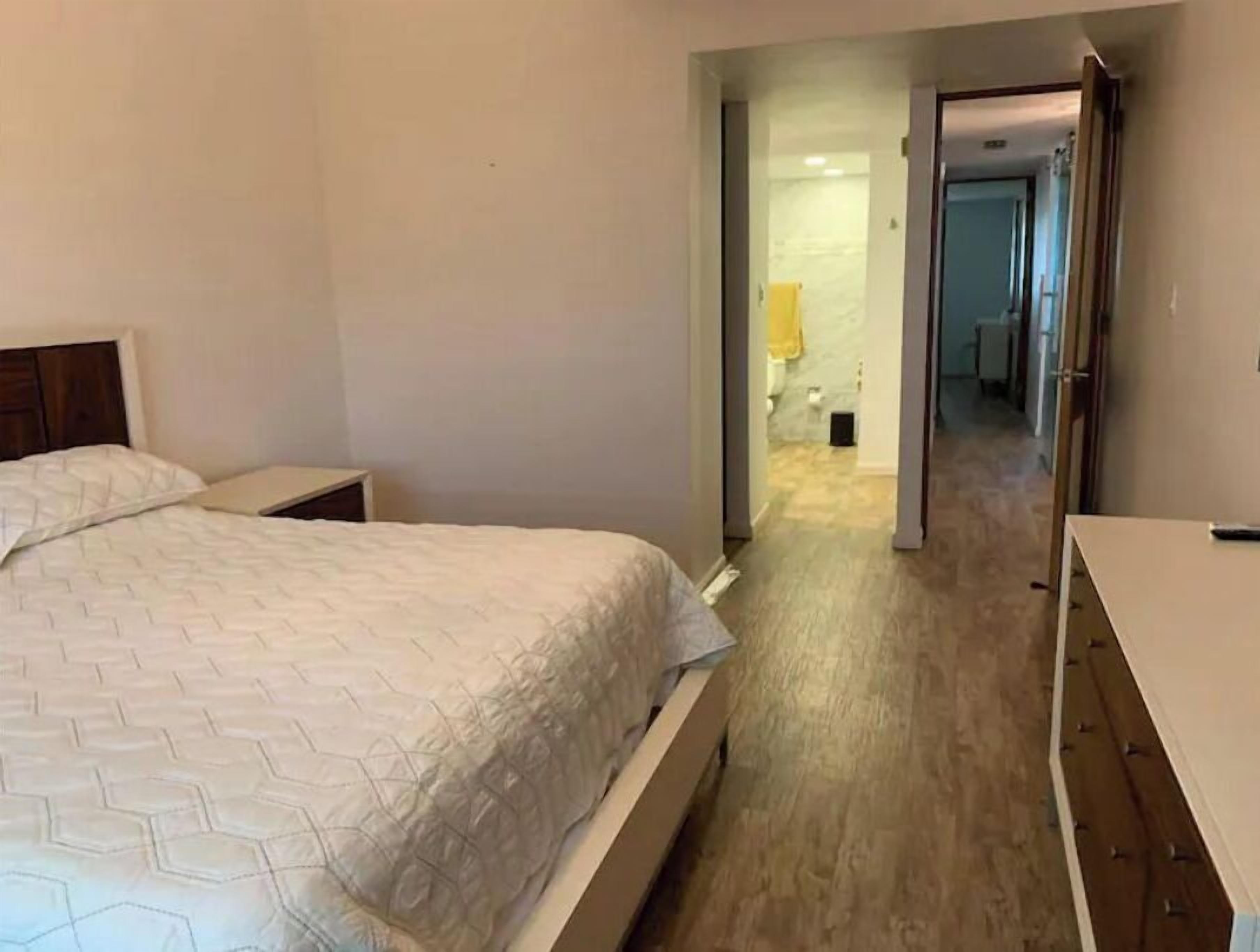 Un dormitorio con cama, mesitas de noche y un pasillo que da a un baño.