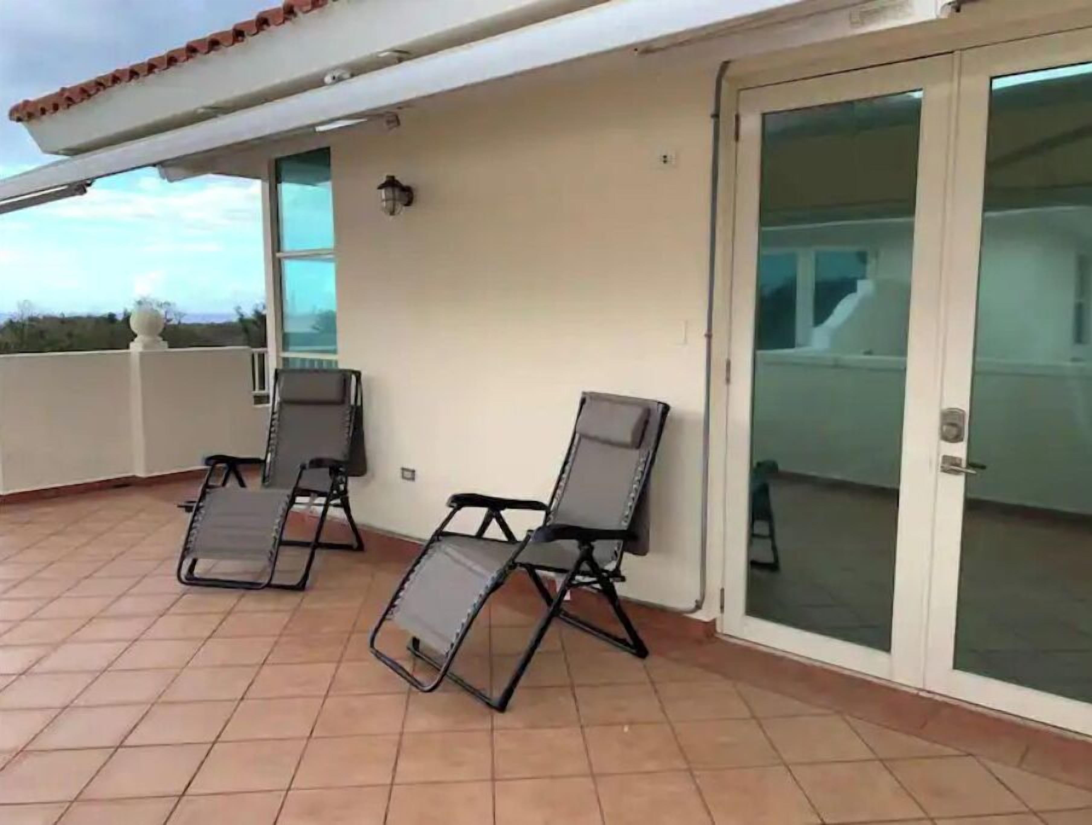 Un balcón con dos sillas reclinables y un ventanal de vidrio que da a un espacio interior.