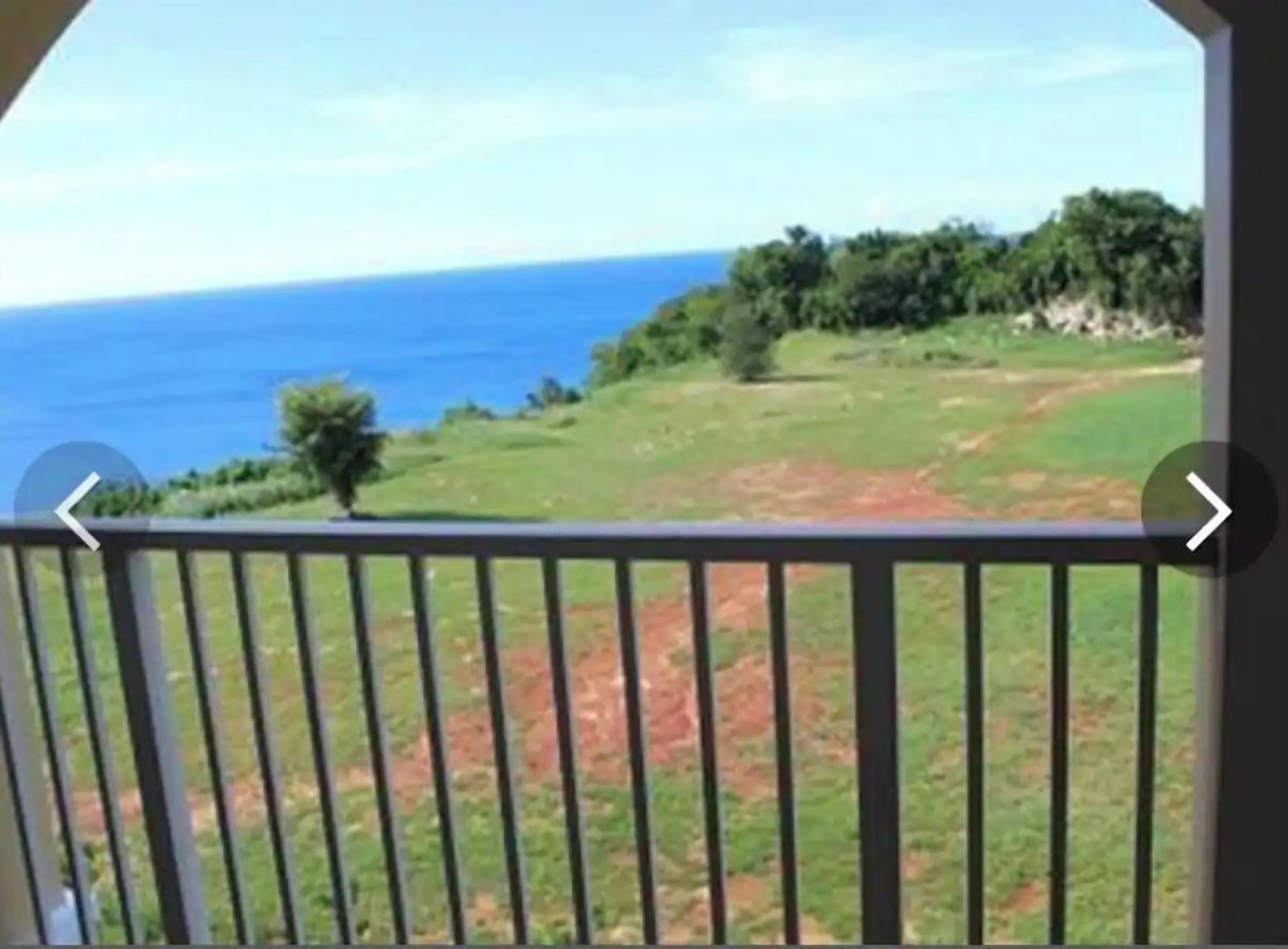 Un balcón con vista al océano y un paisaje con césped.