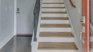 Una escalera de madera con barandilla, que lleva a una puerta en la parte superior.