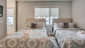 Una habitación de hotel con dos camas, un ventanal grande y un televisor en la pared.