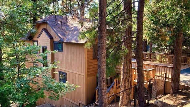 A wooden cabin with a sloped roof, surrounded by trees and a fenced deck area.