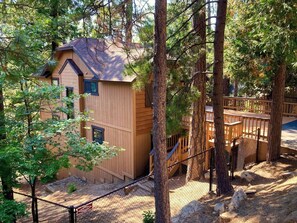 Een houten chalet met schuin dak, omringd door bomen en een omheind terras.