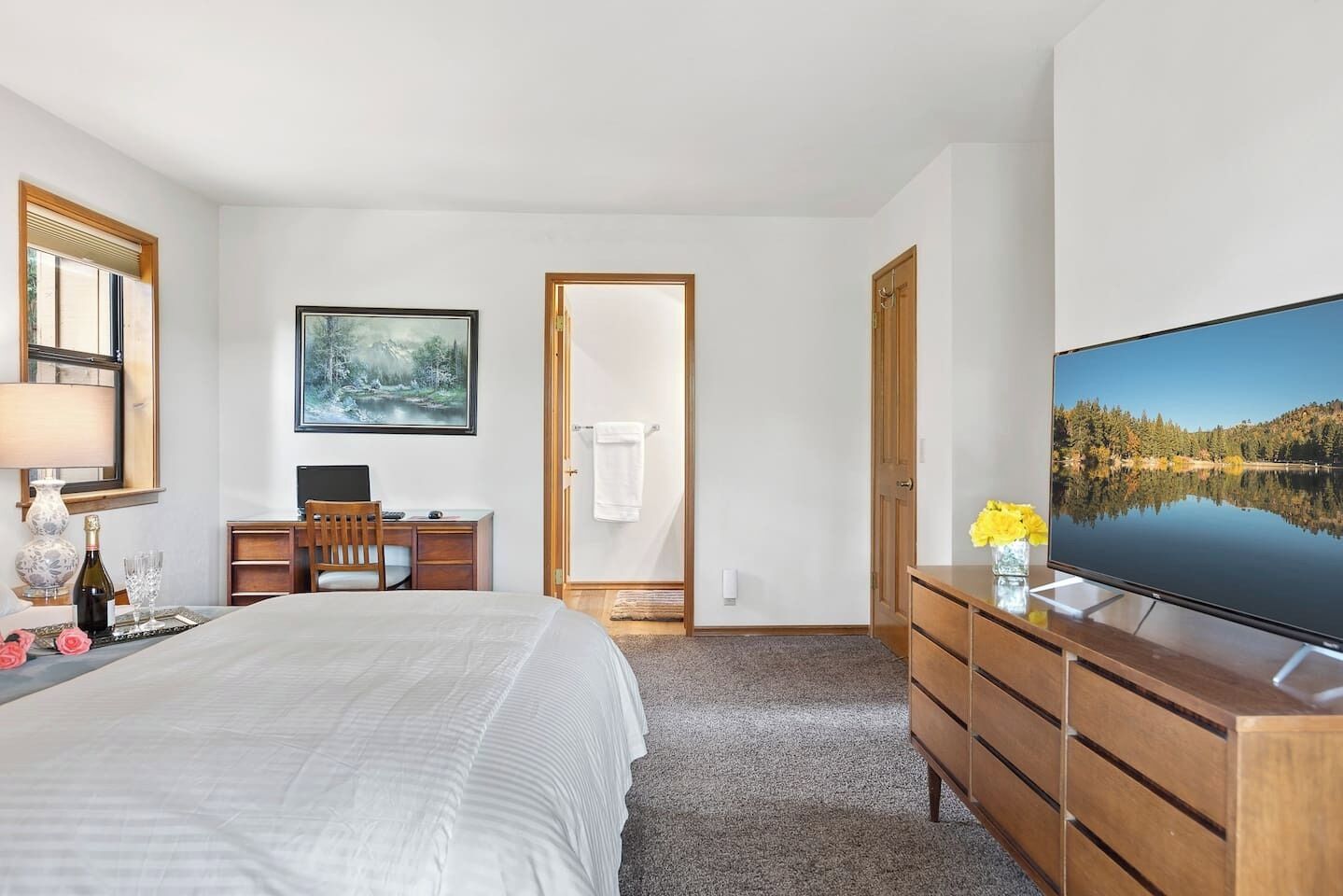 Een slaapkamer met een bed, een bureau met een computer, een televisie en een schilderij aan de muur.