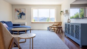 A modern living room with a blue sofa, a tan armchair, a round coffee table, and a blue cabinet with decorative items. - Summit Lofts, Extra Large Executive Suite, #210 (Mt. Shasta)
