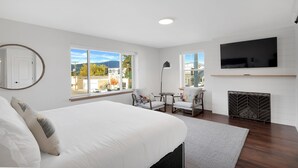 A modern hotel room with a large bed, two armchairs, a small table, a TV, and a fireplace. - Summit Lofts, Extra Large Executive Suite, #210 (Mt. Shasta)