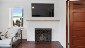 A room with a fireplace, a mounted TV, a window with a view of the outside, and a wooden door. - Summit Lofts, Extra Large Executive Suite, #210 (Mt. Shasta)