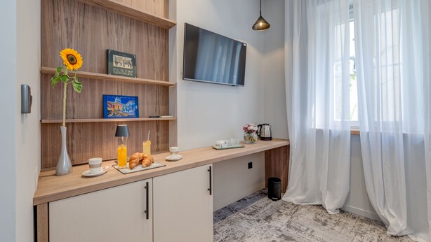 A modern kitchen with wooden shelves, a flat-screen TV, and a large window with sheer curtains. - Makarun Heritage Rooms (Split)