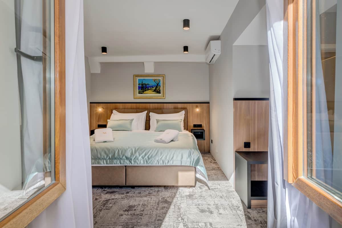 A modern hotel room with a large bed, a wooden headboard, a nightstand, and a framed picture on the wall.