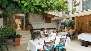 An outdoor dining area with tables and chairs, surrounded by plants and architectural features. - Makarun Heritage Rooms (Split)