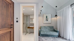 A hallway leading to a bathroom with a sink and shower, a blue sofa, and a painting on the wall. - Makarun Heritage Rooms (Split)