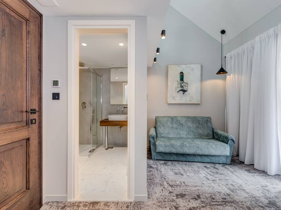 A hallway leading to a bathroom with a sink and shower, a blue sofa, and a painting on the wall.