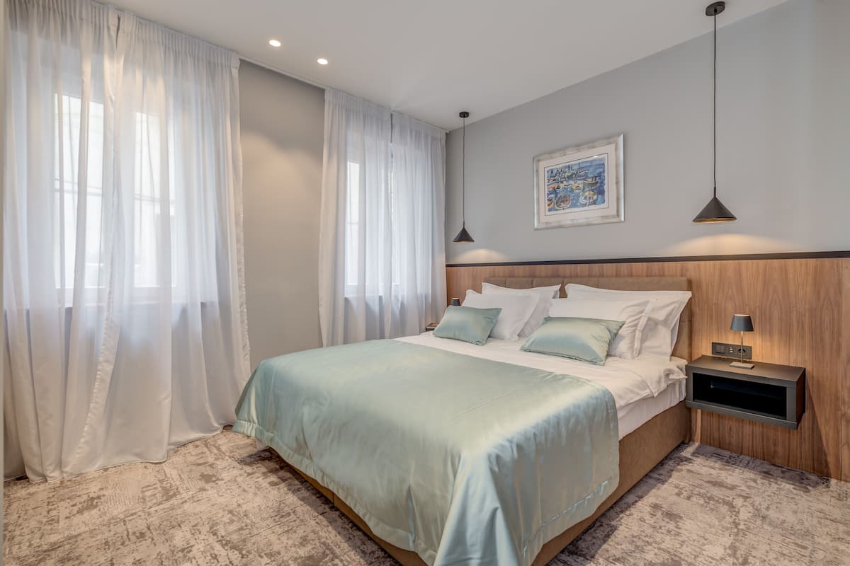 A bedroom with a bed, curtains, a nightstand, and a wall-mounted lamp.