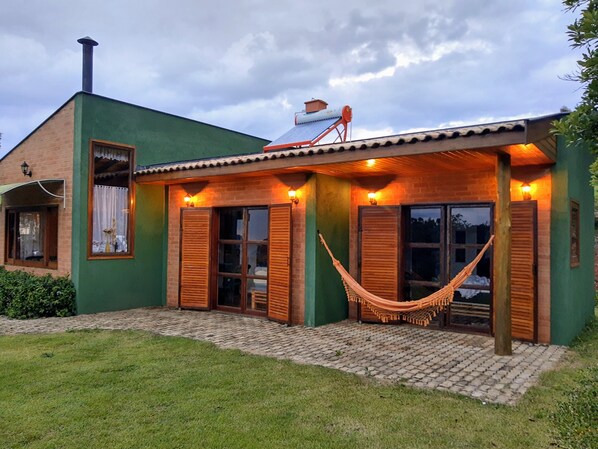 A house with a green exterior, a brick chimney, and a hammock in front.