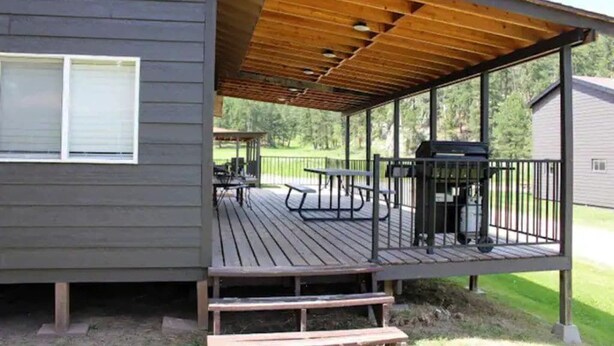 Une terrasse couverte, équipée de tables de pique-nique et d’un barbecue, attenante à une maison dont le revêtement extérieur est de couleur sombre.