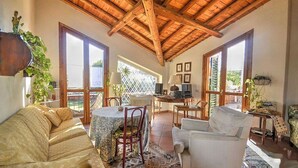 A spacious living room with a high wooden ceiling, large windows, and a cozy seating area with a sofa and armchairs. - Villa With Garden in Sicily Near the sea (Acireale)