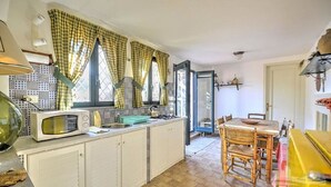 A compact kitchen with a microwave, sink, and wooden dining table. - Villa With Garden in Sicily Near the sea (Acireale)